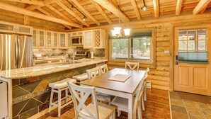 Una cabaña de troncos con cocina equipada, que incluye un refrigerador de acero inoxidable, un microondas y un horno empotrado. Cuenta con un comedor con mesa de madera y sillas blancas.