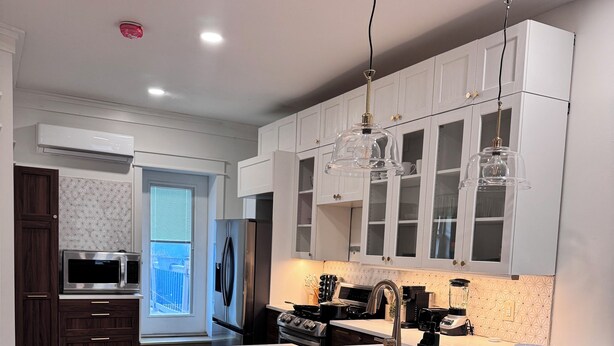 Una cucina moderna con mobili bianchi, un'isola centrale con sgabelli da bar, elettrodomestici in acciaio inossidabile e illuminazione a sospensione.