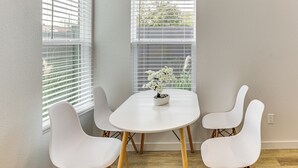 A room with a white table and four white chairs, a potted plant on the table, and a window with blinds. - Great for Travel Nurses: 2BR East Dallas Townhome! (Dallas)
