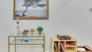 A room with a glass and metal side table, a small wooden shelf, and a framed painting on the wall. - Great for Travel Nurses: 2BR East Dallas Townhome! (Dallas)