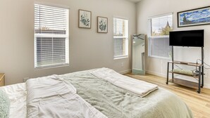 A bedroom with a bed, two windows with blinds, a TV on a stand, and artwork on the wall. - Great for Travel Nurses: 2BR East Dallas Townhome! (Dallas)