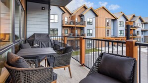 A balcony with wicker furniture, a table, and a view of adjacent buildings. - 3 bedroom + 2 bath -🏔️Rockies Refuge⛰️ heated outdoor pool and hot tub/full gym (Dead Man's Flats)