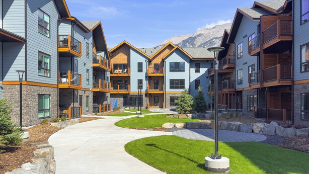 A modern multi-story residential building with balconies, a central courtyard, and a mountain backdrop. - 3 bedroom + 2 bath -🏔️Rockies Refuge⛰️ heated outdoor pool and hot tub/full gym (Dead Man's Flats)