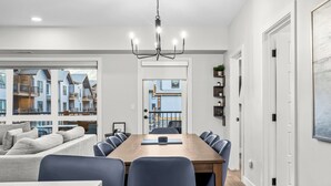 A modern dining area with a long wooden table, blue chairs, and a chandelier. - 3 bedroom + 2 bath -🏔️Rockies Refuge⛰️ heated outdoor pool and hot tub/full gym (Dead Man's Flats)