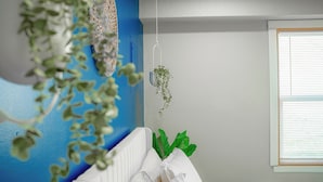 Et værelse med en blå accentvæg, en hvid barneseng og hængende planter.