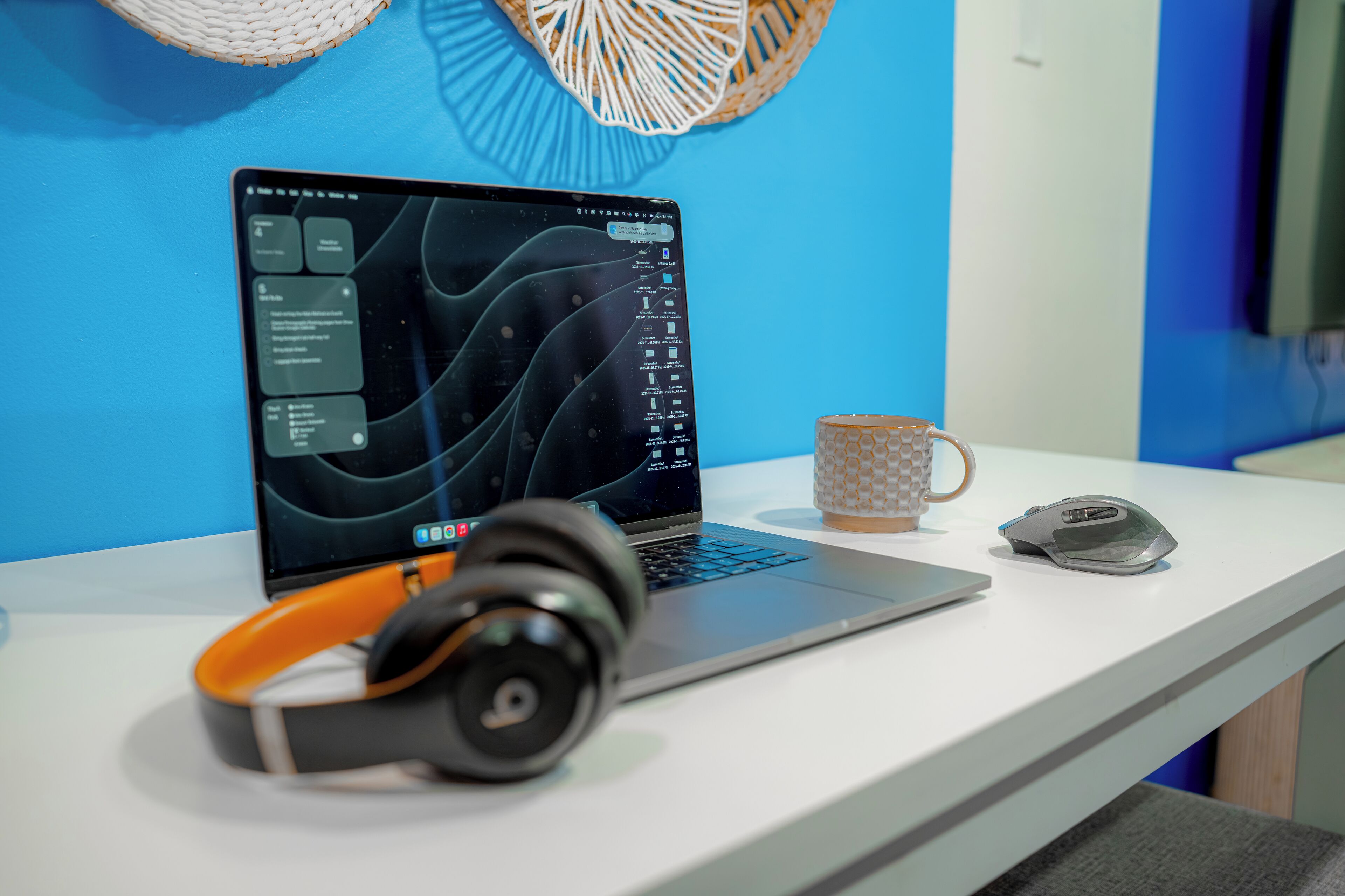 Een laptop op een wit bureau, met een koptelefoon, een muis en een koffiemok.