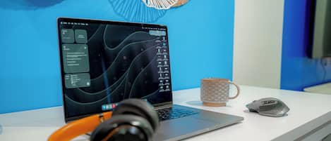 A laptop on a white desk with a pair of headphones, a mouse, and a coffee mug.