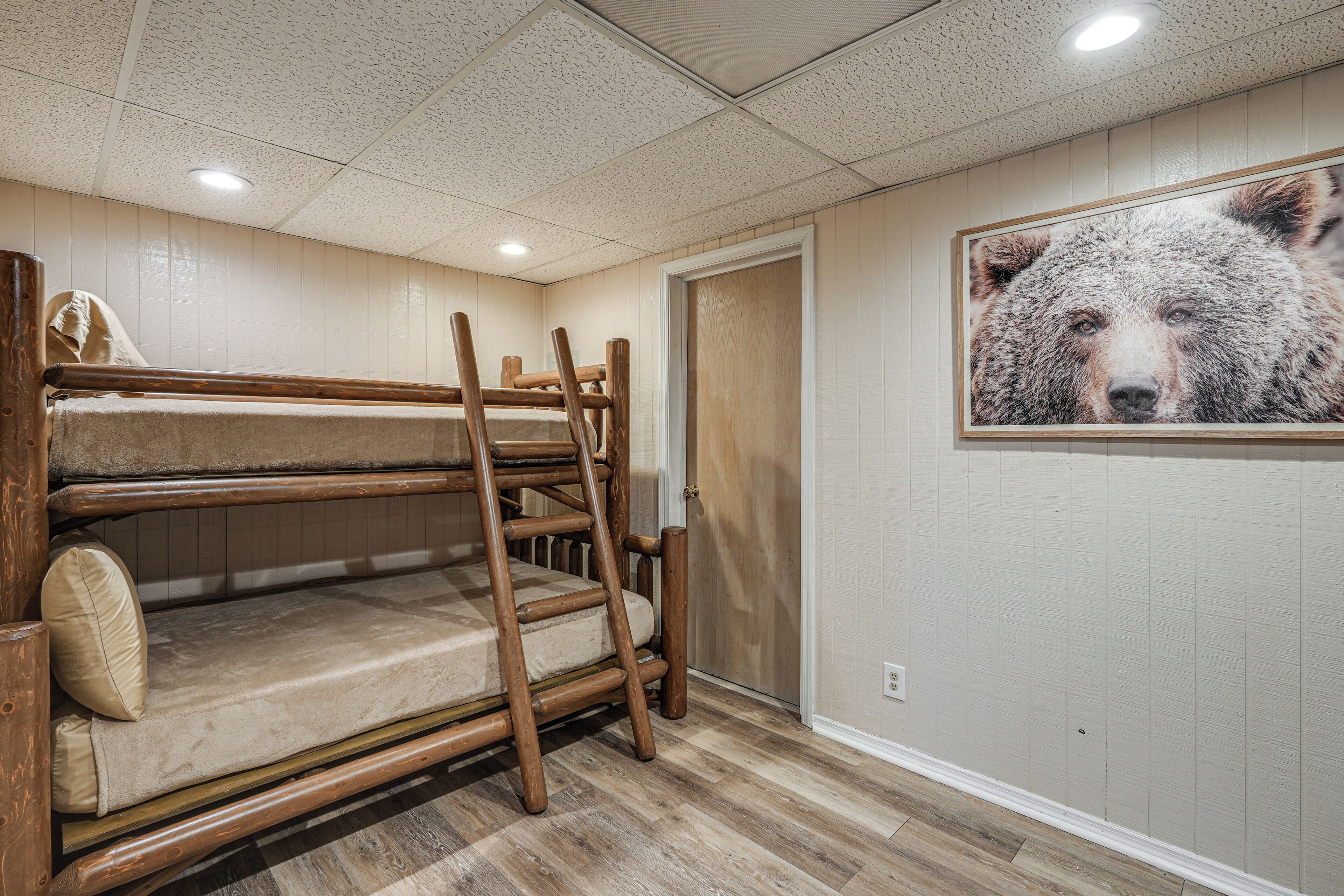 A bunk bed with a ladder, a wooden door, and a framed bear picture on the wall.