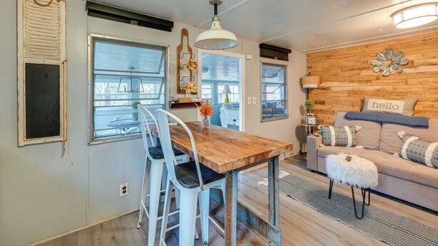 A dining area with a wooden table and white chairs, a hanging light fixture, and a wooden wall with a flower decoration. - Lake Malone Cabin Getaway! Dock, Fire Pit, Grill (Dunmor)