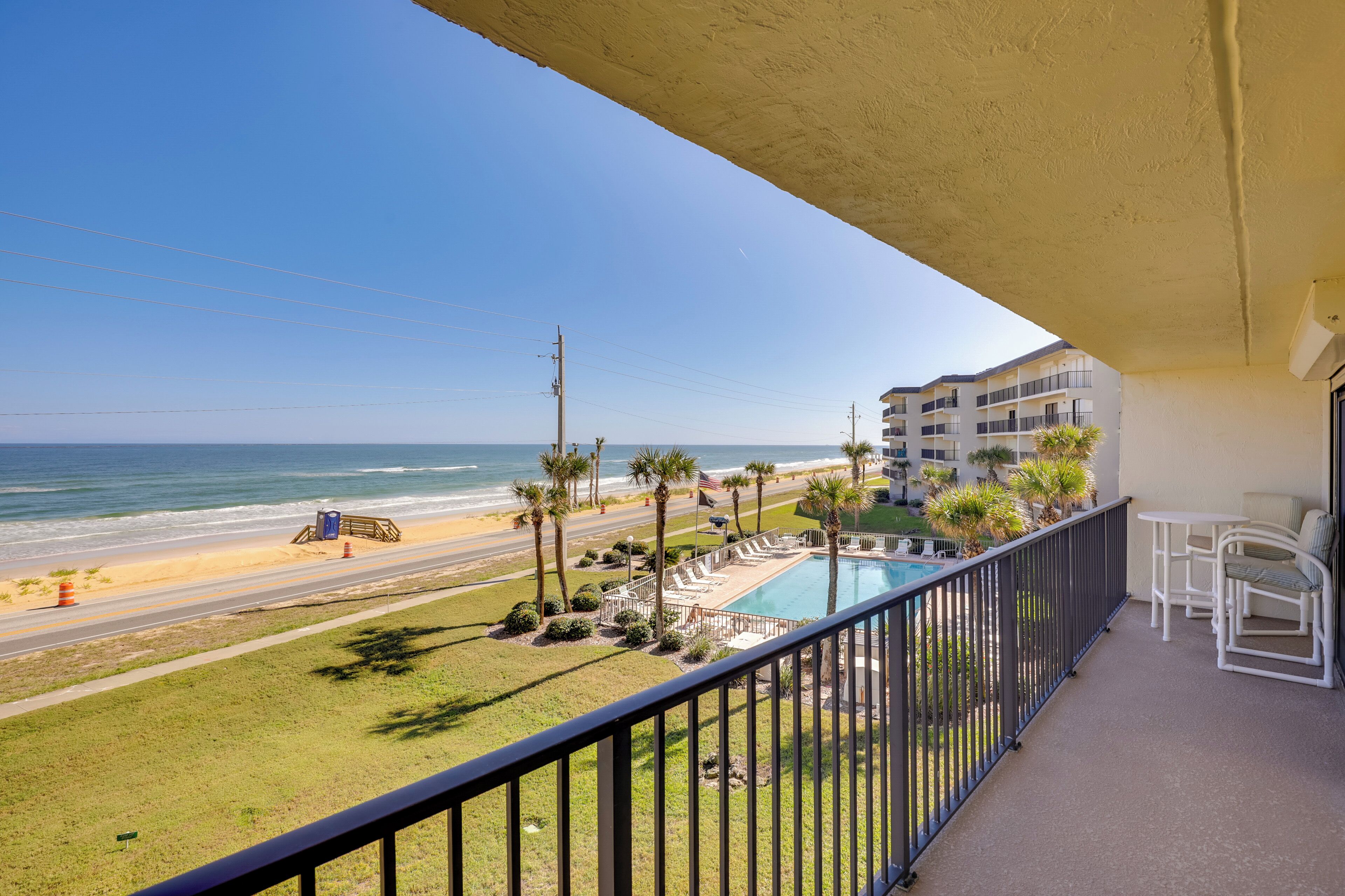 A balcony with a view of the beach, a pool, and a road.