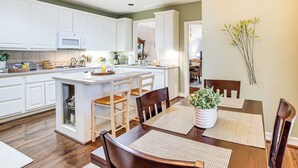 A modern kitchen with white cabinetry, a central island, and a dining area with wooden chairs and a table. - Uptown Dallas Group Getaway Near Art, Eats & More! (Dallas)
