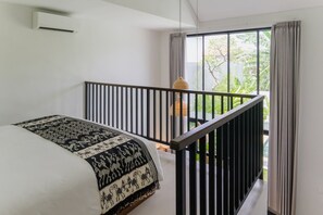 A bedroom with a bed, a window with curtains, a hanging light, and a balcony railing. - Sunset Loft Seminyak, Bali (Seminyak)