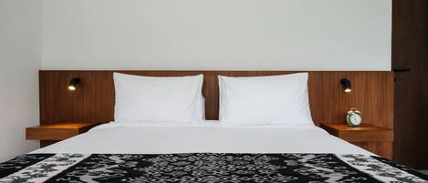 Un lit avec une couvre-lit à motifs, une tête de lit en bois, deux oreillers blancs, des tables de chevet avec des lampes et un petit réveil vert.