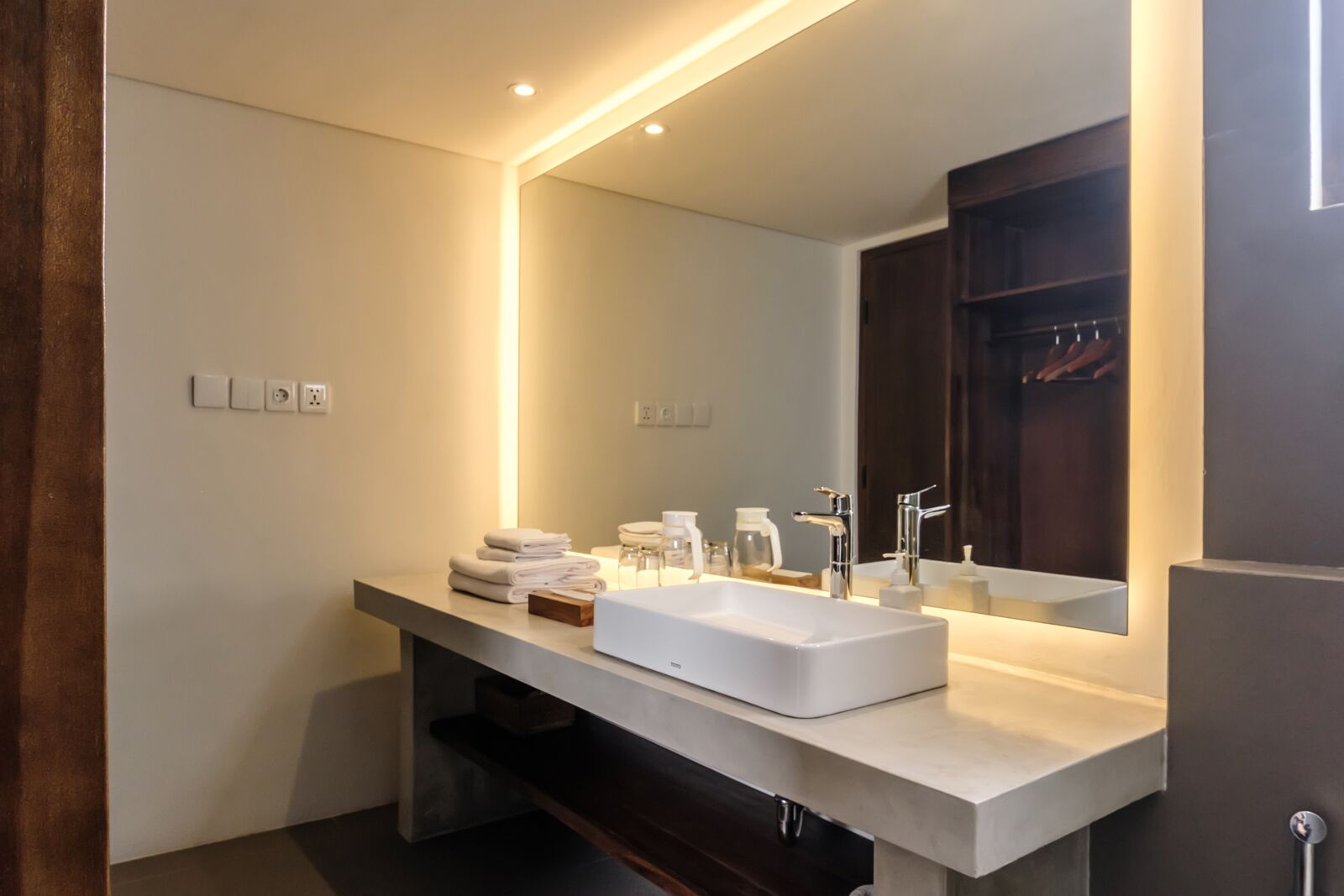 A modern bathroom with a large sink, mirror, and dark wooden cabinet.