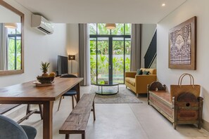 A modern living room with a wooden dining table, a sofa, and a staircase leading to a balcony. - Sunset Loft Seminyak, Bali (Seminyak)