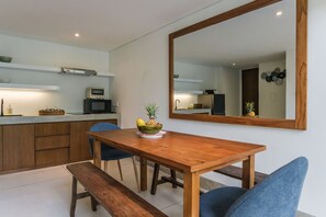A modern kitchen with a wooden dining table, chairs, and a large mirror. - Sunset Loft Seminyak, Bali (Seminyak)