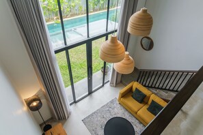 A modern interior with a yellow sofa, large windows, and a pool view. - Sunset Loft Seminyak, Bali (Seminyak)