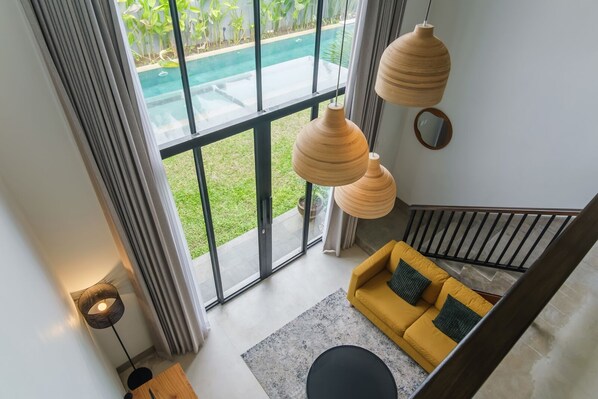 A modern interior with a yellow sofa, large windows, and a pool view. - Sunset Loft Seminyak, Bali (Seminyak)