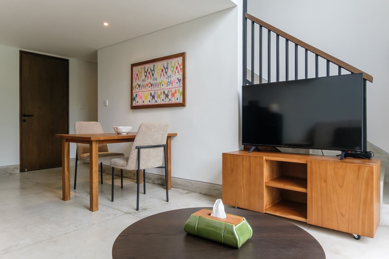 Un salon moderne avec un meuble TV en bois, un téléviseur à écran plat, une table à manger avec des chaises et un tableau accroché au mur.