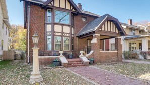 A two-story house with a brick facade, large windows, and a front porch with steps leading to the entrance. - Historic Home Overlooking Central Riverside Park! (Wichita)