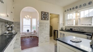 A modern kitchen with white cabinets, a black countertop, and a dining area with a chandelier. - Historic Home Overlooking Central Riverside Park! (Wichita)