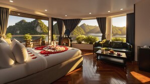 A spacious bedroom with a large bed, a sofa, a coffee table, and a view of a mountainous landscape. - Aqua Luxury Cruise (Tuan Chau)