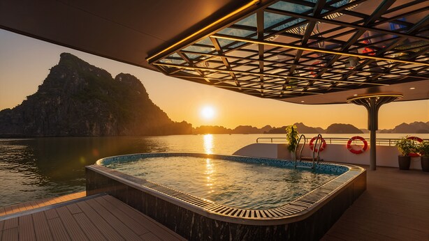 A hot tub on a deck with a view of a sunset over water and mountains. - Aqua Luxury Cruise (Tuan Chau)