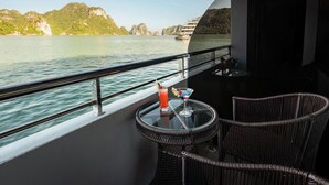 A balcony with wicker chairs and a table, overlooking a body of water with distant landforms. - Aqua Luxury Cruise (Tuan Chau)