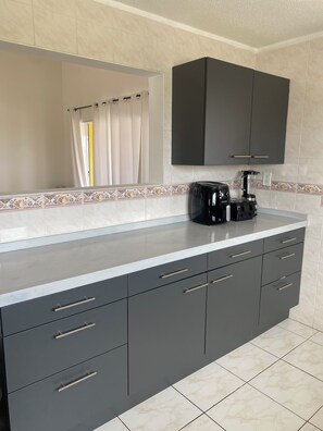 A modern kitchen with dark grey cabinets, a white countertop, and a coffee maker. - Bendishon Villa - 5 Bedroom Villa (Grote Berg)