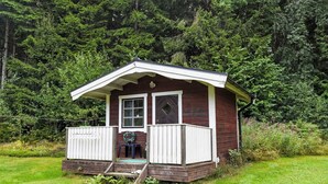 Une petite cabane en bois dotée d’un porche, entourée d’une forêt dense.