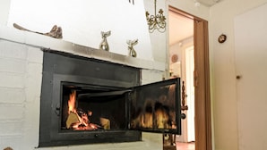 Une cheminée avec un feu qui crépite à l’intérieur, un mur en briques blanches et un plancher en bois.