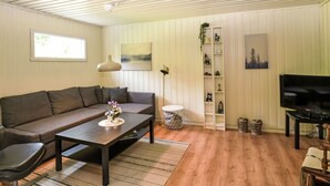 Un salon comprenant un canapé, une table basse, un téléviseur et des étagères ornées d’objets décoratifs.