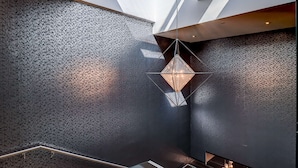 Un interior moderno con una pared texturizada, un aplique geométrico y una barandilla de vidrio.