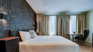 A modern hotel room with a large bed, a desk, and a chair. - Dream Suites - Deluxe King Suite (MISSISSAUGA)