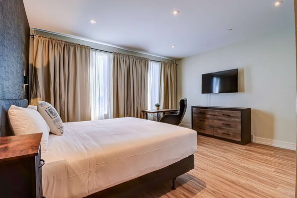 A hotel room with a bed, a desk, a chair, a TV, and a dresser.