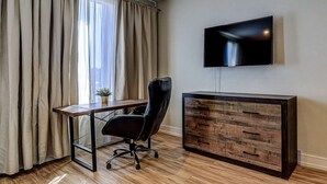 A modern room with a wooden desk, black office chair, and a TV mounted on the wall. - Dream Suites - Deluxe King Suite (MISSISSAUGA)