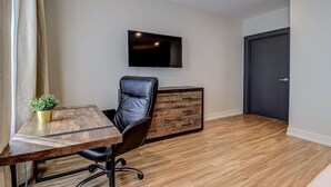 A modern room with a wooden desk, a leather chair, a flat-screen TV mounted on the wall, and a dark door. - Dream Suites - Deluxe King Suite (MISSISSAUGA)