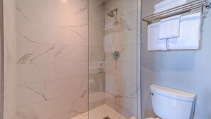 Un baño con ducha de vidrio, baldosas de mármol, inodoro y toallero con toallas dobladas.