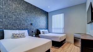 A hotel room with two beds, a patterned wall, a window with blinds, and a wooden floor. - Dream Suites - Deluxe Family  Suite (MISSISSAUGA)