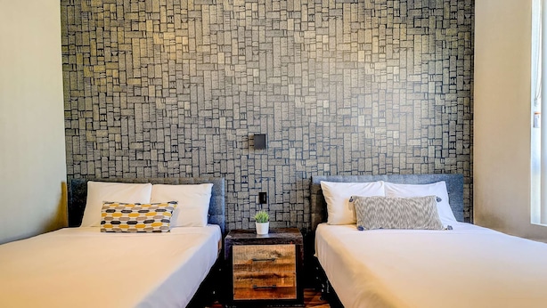 A room with two beds, a small wooden nightstand, and a patterned wall. - Dream Suites - Deluxe Family  Suite (MISSISSAUGA)