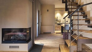 Um interior moderno com lareira, piso de madeira e escada com guarda-corrimão de metal.