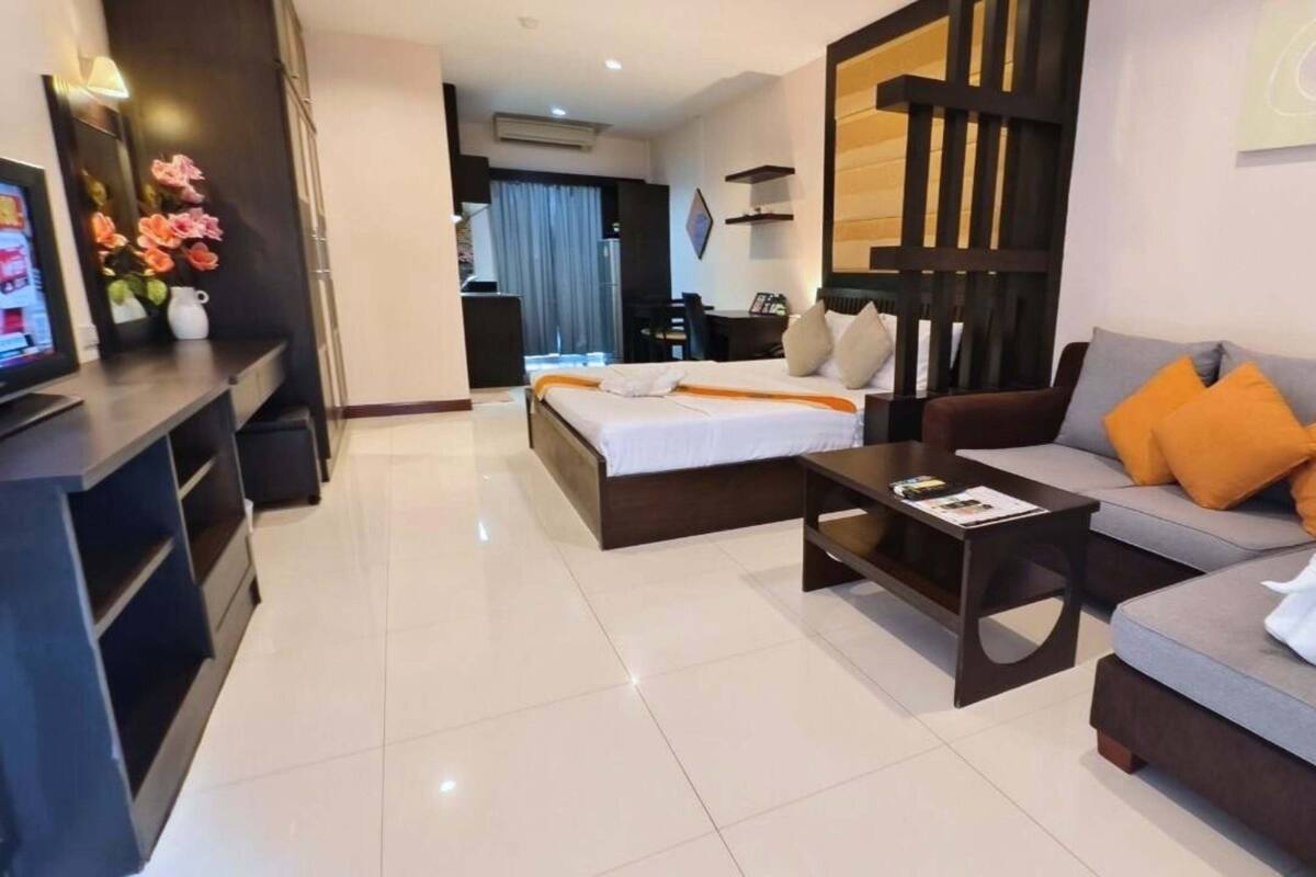 A modern hotel room with a bed, sofa, and a TV on a desk.