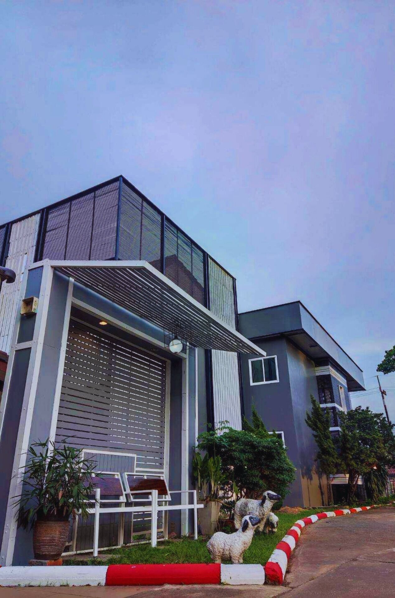 A modern building with a large garage door, a covered entrance, and a small garden area with a statue.