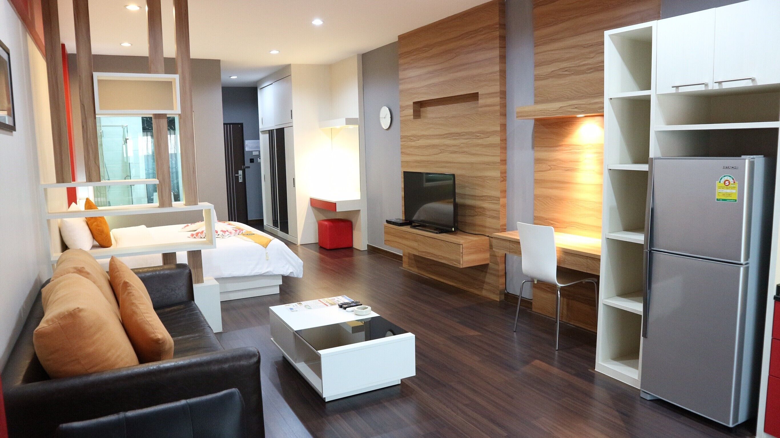 Une chambre d’hôtel moderne équipée d’un canapé, d’une table basse, d’une télévision, d’un réfrigérateur et d’un mur décoratif en bois.