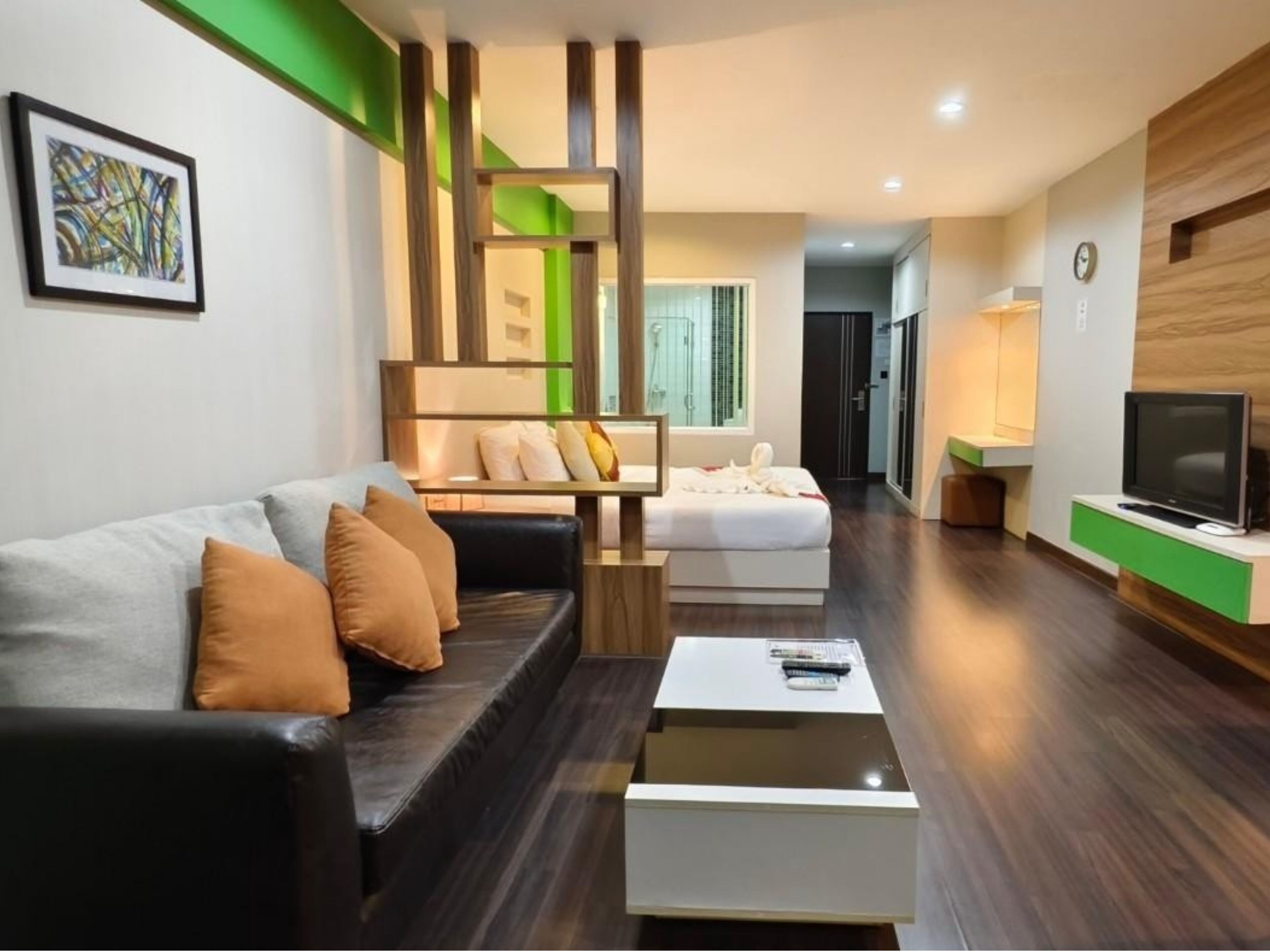 Una sala moderna con un sofá, una mesa de centro y un televisor. Se observa un dormitorio separado al fondo.