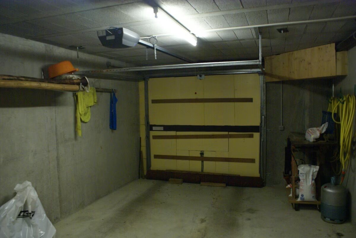 Un garaje con puerta cerrada, paredes de concreto, un ventilador de techo y algunos productos de limpieza en estantes.