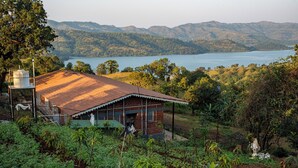 A rustic building with a metal roof, surrounded by lush greenery and a lake in the background. - Cosmicstays Birdsong Lakeview Cottage  (Velhe)