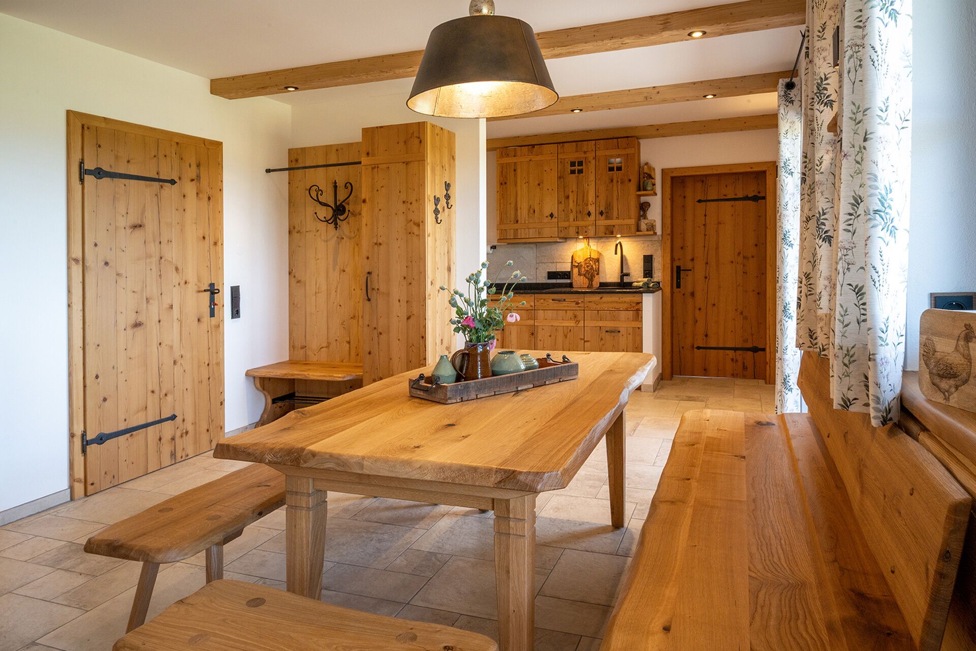 A wooden interior with a central table, benches, and a hanging light fixture.