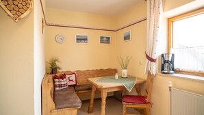 A cozy corner with a wooden bench, a table with a green tablecloth, a coffee maker, and a window with curtains. - Vacation apartment lake view (Kirchanschöring)