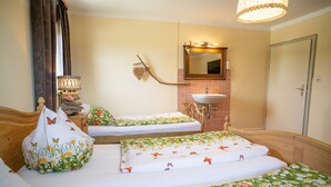 A hotel room with two single beds, a bedside table with a lamp, a wall-mounted mirror, a sink, and a door. - Vacation apartment lake view (Kirchanschöring)